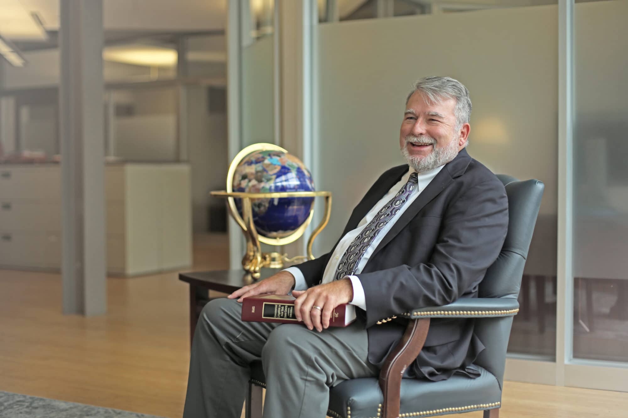 Donald S. DiBenedetto wearing a dark jacket and tie, smiles in the middle of discussion while sitting in a leather chair in Costello, Cooney & Fearon's Hall of Justice