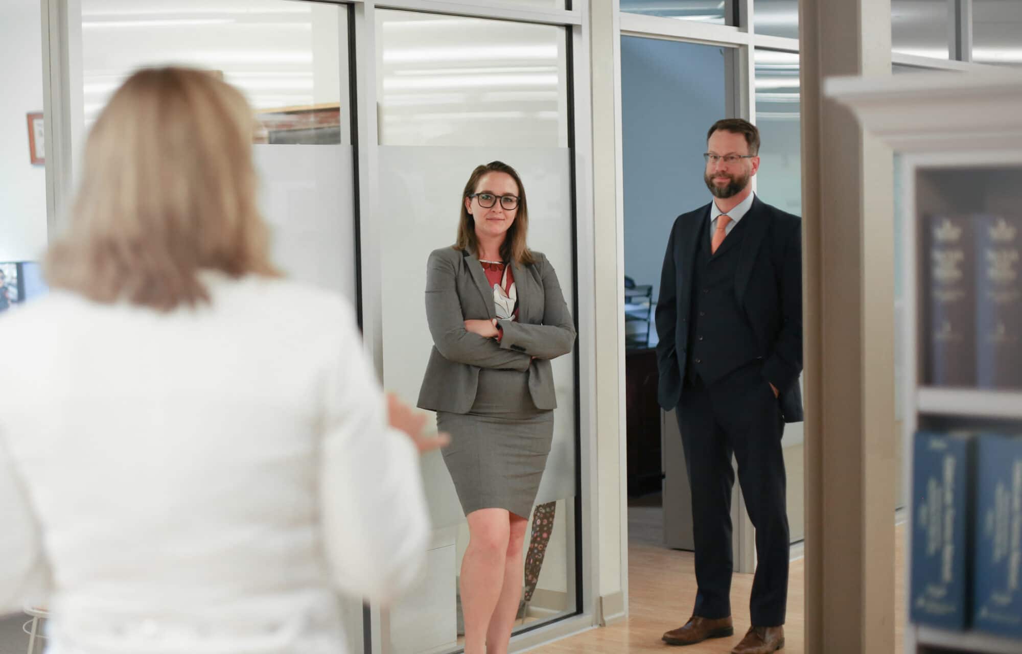 Stacy Marris and John Langey speaking with partner Nadine Bell in the Costello law offices, with book cases full of legal books to the side of the composition, and glass panel doors in the distance